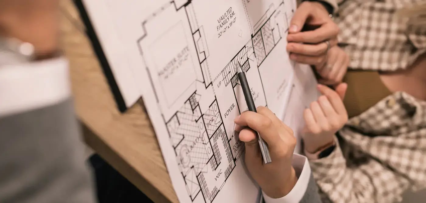 A man and woman examine a floorplan together, engaged in discussion and pointing to specific details on the plan.