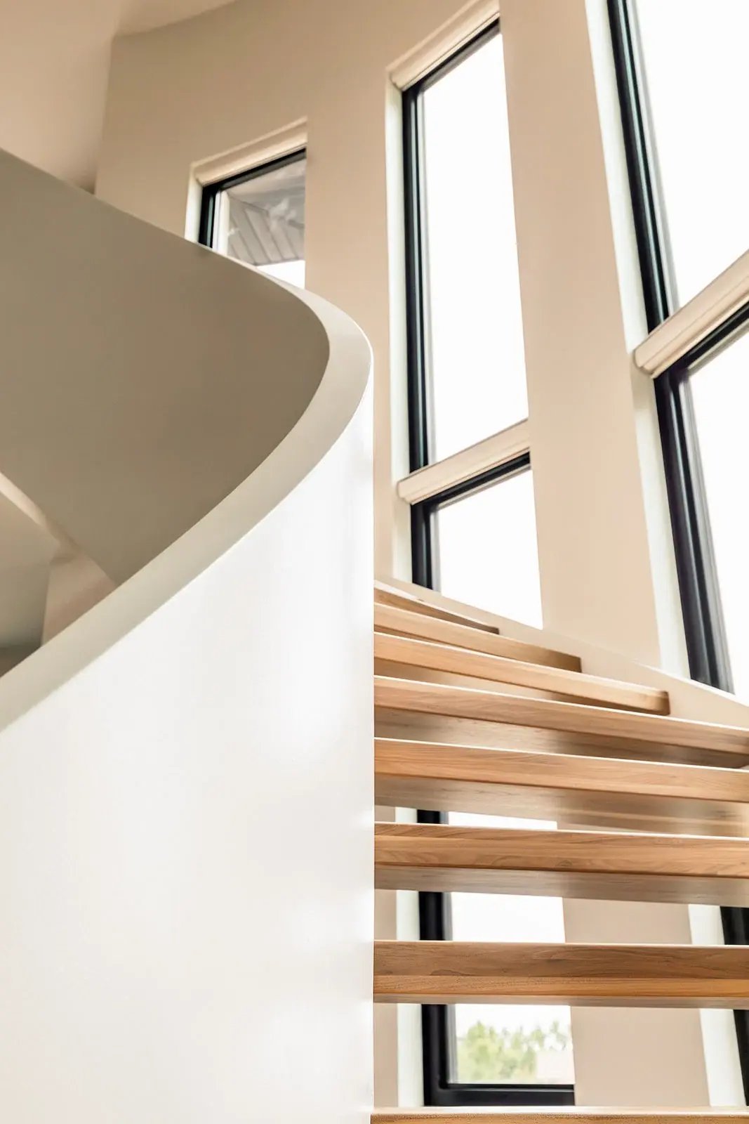 Curved staircase with oak treads beside tall windows